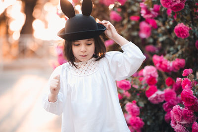 Cute stylish child girl 5-6 year old wear trendy clothes and hat posing over flower rose outdoors 