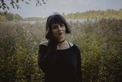 Portrait of young woman standing on field against sky