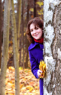 Portrait of smiling woman standing by tree trunk in forest