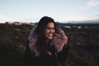 Smiling woman in warm clothes standing outdoors during sunset