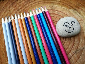 High angle view of stone with anthropomorphic face by colored pencils on wooden table