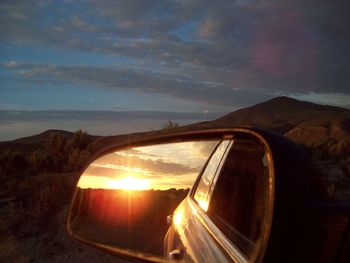 Reflection of illuminated side-view mirror against sky at sunset