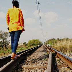 Rear view of man standing on railroad track against sky