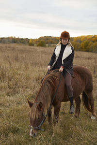 Portrait of young woman riding horse on field