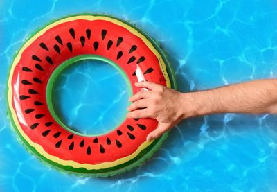 Cropped hand of man holding inflatable ring floating on swimming pool