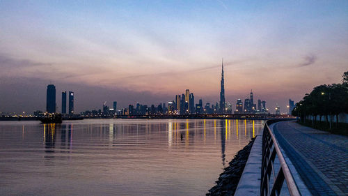 Scenic view of river by buildings against sky during sunset