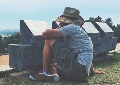 Full length of man reading information sign on wood while sitting at field