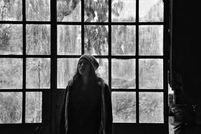 Thoughtful woman looking up while standing against window