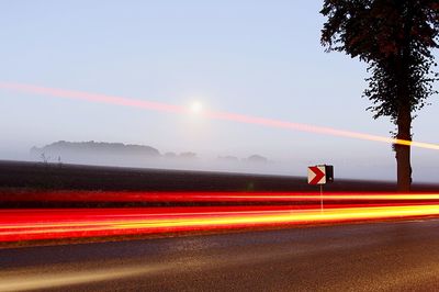 Light trail on highway against sky at foggy dawn
