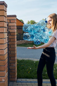 Young woman throwing out empty used plastic water bottles into trash bin. collecting plastic waste