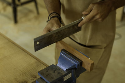 Midsection of man cutting wood with saw