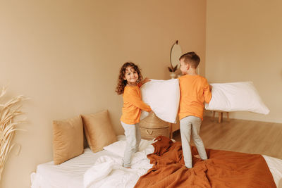 Funny  kids brother and sister in pajamas playing fighting with pillows in a cozy bedroom at home