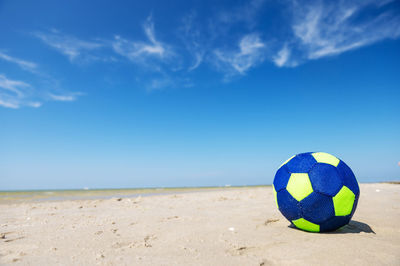 Blue ball on sand at beach against sky