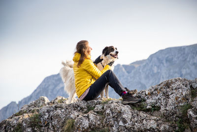 Woman sitting on rock against mountain range against clear sky