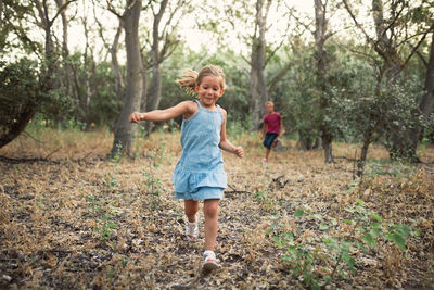 Siblings running on land in forest against trees
