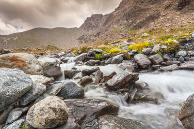 Scenic view of stream flowing through rocks against sky