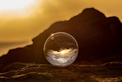 Close-up of crystal ball on rock against sky during sunset