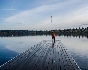 Man standing on jetty by lake against sky