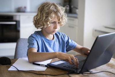 Boy with blond hair using laptop on table at home