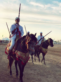 Men riding horses on street against sky