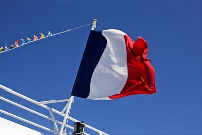 Low angle view of french flag on railing against clear blue sky