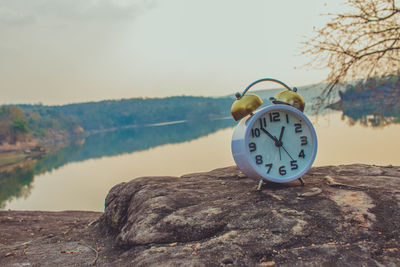 Alarm clock on cliff against lake