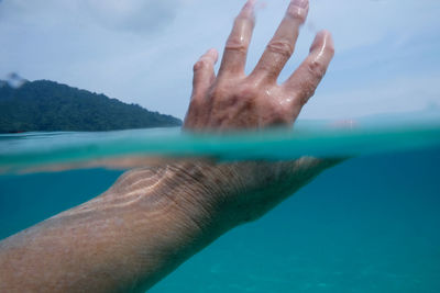 Midsection of man surfing in sea against sky