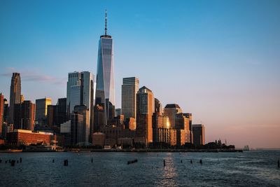 Sea by modern buildings against sky during sunset