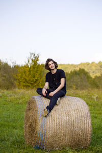 Portrait of smiling young man sitting on hay bale at field
