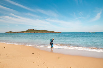 Rear view of woman walking at beach against sky