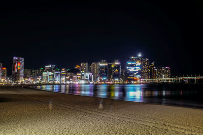 Illuminated buildings by river against sky at night