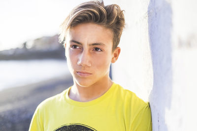 Thoughtful teenage boy looking away by wall