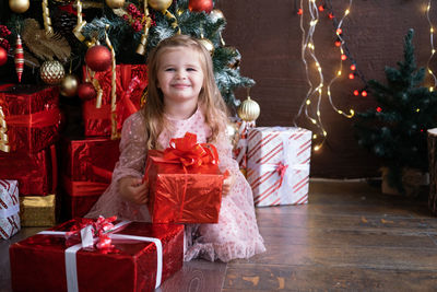 Portrait of smiling girl holding gift box sitting at home