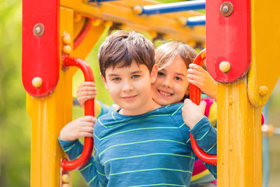 Smiling cute boy and girl, brunettes, stand among the yellow colorful playground