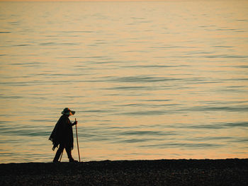 Man photographing on shore against sky during sunset