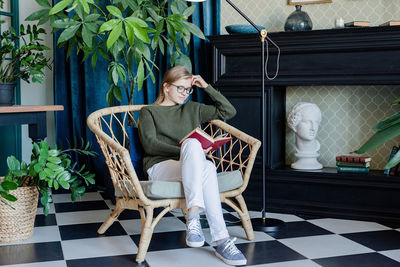 Leisure time. young blonde woman sitting in comfortable chair reading a book surrounded with plants