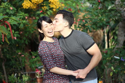 Young couple kissing while standing against plants