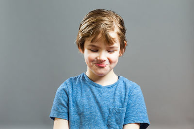 Playful boy making face against gray background