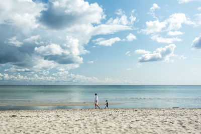 Side view of people walking at beach against sky