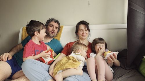 Happy parents reading a book to children sitting in the bed