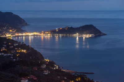 Illuminated city by sea against sky at night