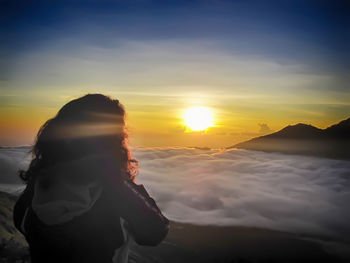 Rear view of woman looking at cloudscape over mountains during sunset