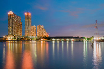 Illuminated buildings by river against sky at night