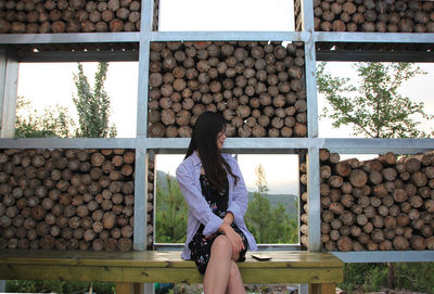 Woman sitting on bench against stacked logs