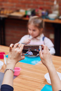 Mother photographing girl in baking workshop on smart phone