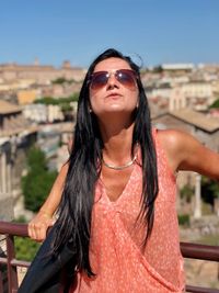 Young woman wearing sunglasses standing against cityscape