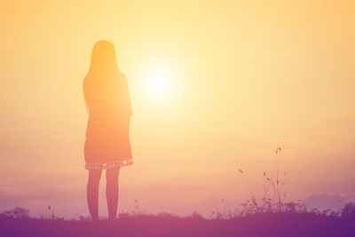 Rear view of silhouette woman standing on field during sunset