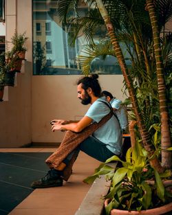 Side view of young man using smart phone while sitting by plants