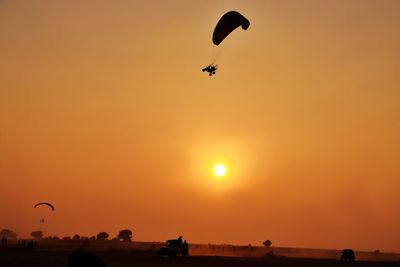 Silhouette person paragliding against orange sky