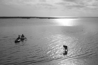 Silhouette people swimming in sea against sky